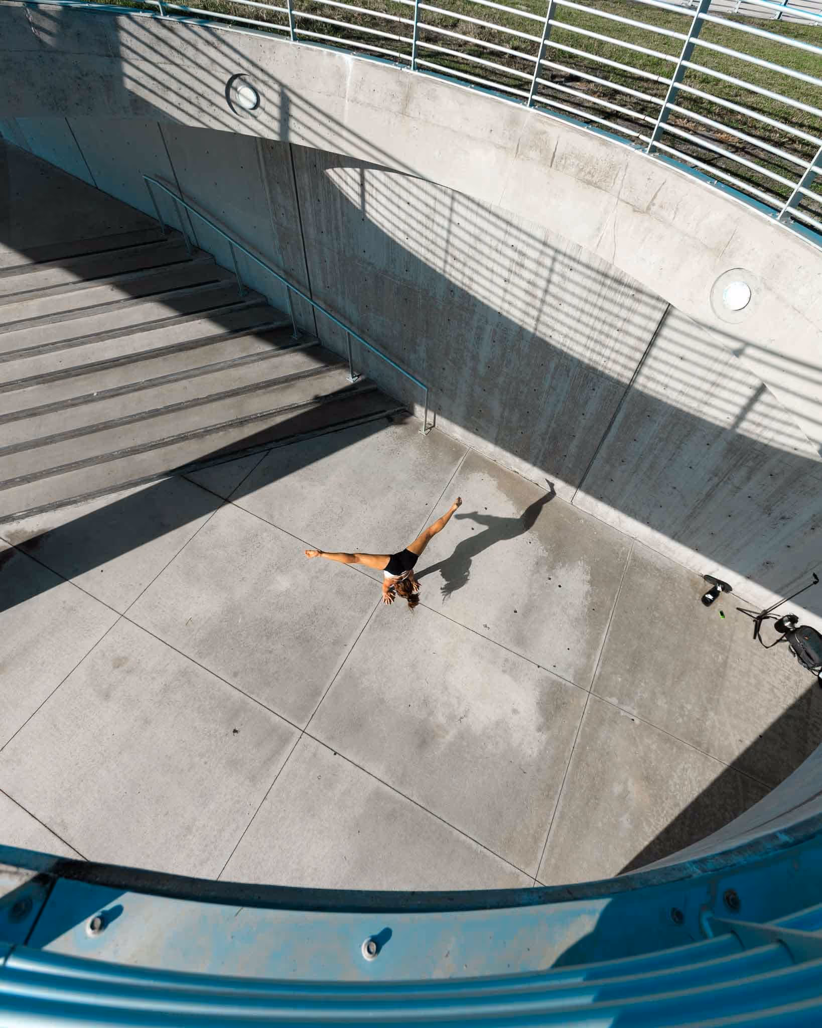 Overhead view of Selena in a straddle handstand on a wide concrete plaza